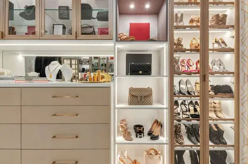 A modern, well-organised custom walk-in wardrobe featuring light wood cabinetry, built-in drawers, dedicated shoe shelving, and various hanging sections for clothing.