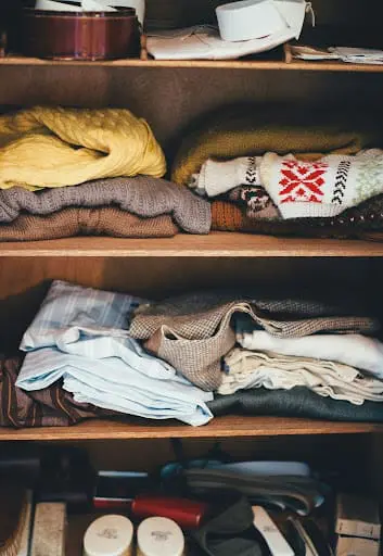 Close-up of organized wooden wardrobe shelves featuring neatly folded sweaters and clothing in neutral tones.