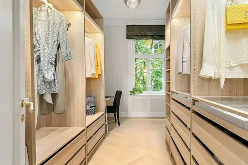A modern, well-lit walk-in closet featuring custom timber-look cabinetry, organized hanging sections for clothing, and built-in drawers
