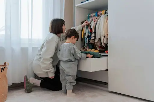 A mother and young child organizing clothes together in a modern, well-lit walk-in wardrobe with custom shelving.