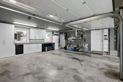 A clean, modern garage featuring custom grey cabinetry and overhead wire shelving units for organized storage.